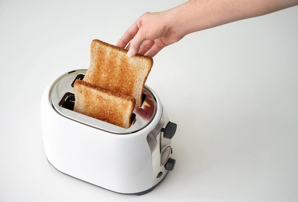 Woman taking bread slice from toaster on table - 写真・画像