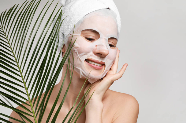 Woman with sheet facial mask and tropical leaf on light background - Foto, Imagem