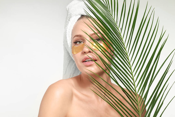 Young woman with under-eye patches and tropical leaf on white background - Photo, Image