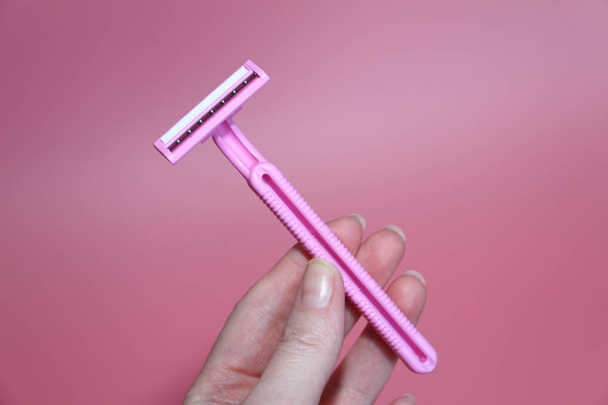 Pink razor in a beautiful female hand. Pink background. - Valokuva, kuva