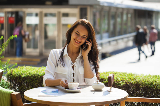 Elegant girl calling someone while resting in outdoor cafe with  - Foto, Bild