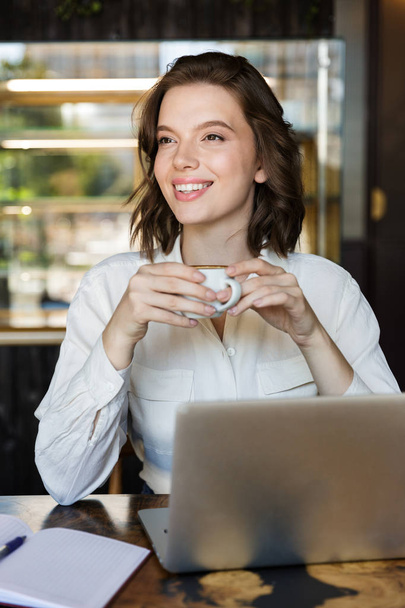 Sonriente joven mujer de negocios sentada en el café en el interior
 - Foto, Imagen