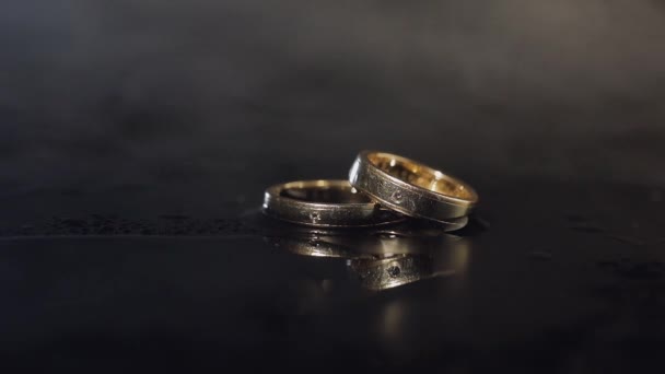 Свадебные кольца, лежащие на темной поверхности, сияют светом крупным планом
 - Кадры, видео