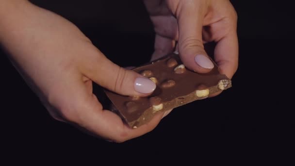 Vrouw einden zwarte chocolade reep met noten. Close-up. Slow motion - Video