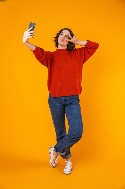 Excited emotional young pretty woman posing isolated over yellow wall background take selfie by mobile phone. - Фото, зображення