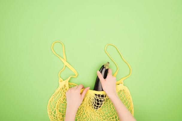 vista ritagliato di donna mettendo melanzane in sacchetto di stringa giallo su sfondo verde chiaro
 - Foto, immagini
