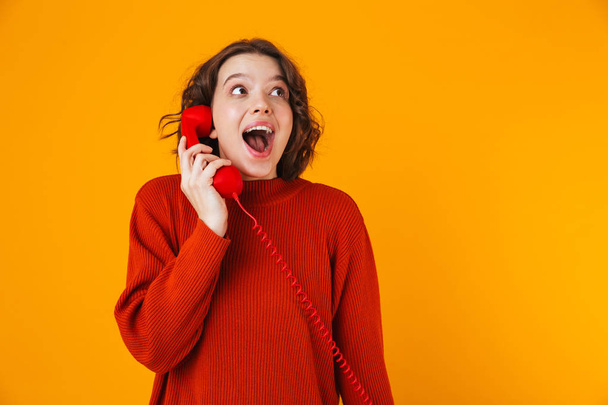 Emotional young pretty woman posing isolated over yellow wall background talking by telephone. - Photo, Image