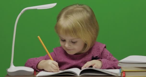 Meisje tekenen aan de tafel. Onderwijsproces in klas. Gelukkig drie jaar oud meisje. Schattig meisje glimlachend. Mooi klein kind, 3-4 jaar oud blond meisje. Maken van gezichten. Groen scherm video. Chromakey - Video