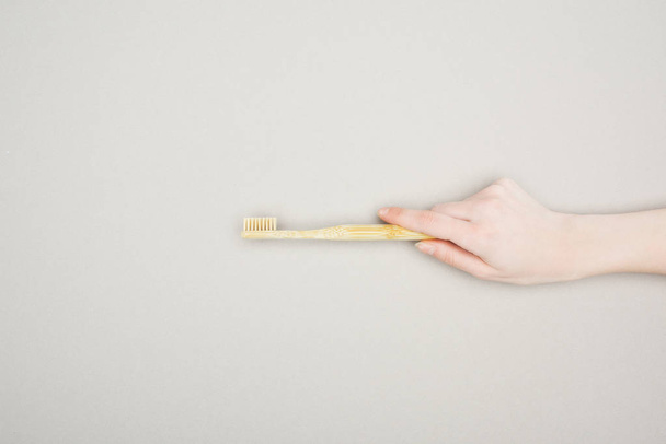 vista recortada de la mujer sosteniendo el cepillo de dientes de bambú sobre fondo gris
 - Foto, Imagen
