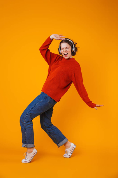 Emotional young pretty woman posing isolated over yellow wall background listening music with headphones. - Foto, imagen