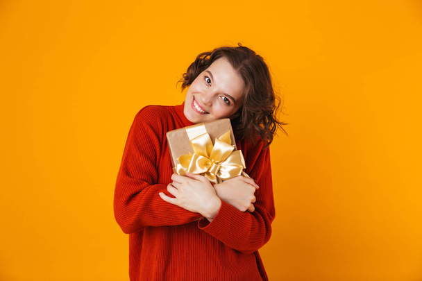 Emotional young pretty woman posing isolated over yellow wall background holding present gift. - Foto, afbeelding