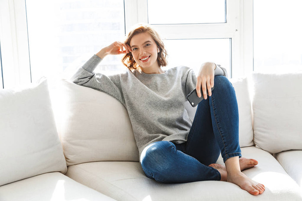 Beautiful smiling young woman relaxing on a couch - Фото, изображение