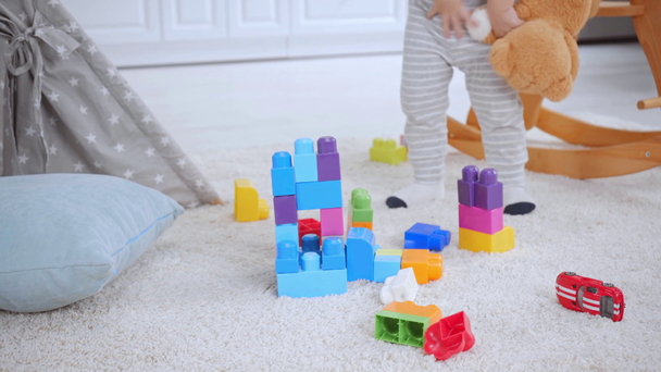 cropped view of boy with teddy bear standing on carpet near building blocks - Footage, Video