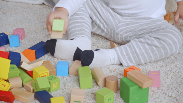 adorable chico emocional sentado en la alfombra y jugando con bloques de madera de colores
 - Imágenes, Vídeo