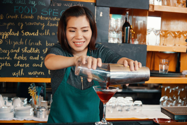 Улыбающийся бармен наливает коктейль из шейкера в бокал маргариты
  - Фото, изображение