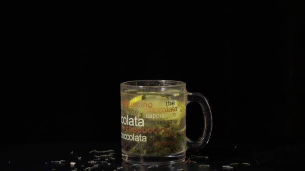 Green tea. Glass cup with organic dry green tea leaves and slice of lemon which are floating inside cup in hot water. Slow motion. Black background - Footage, Video
