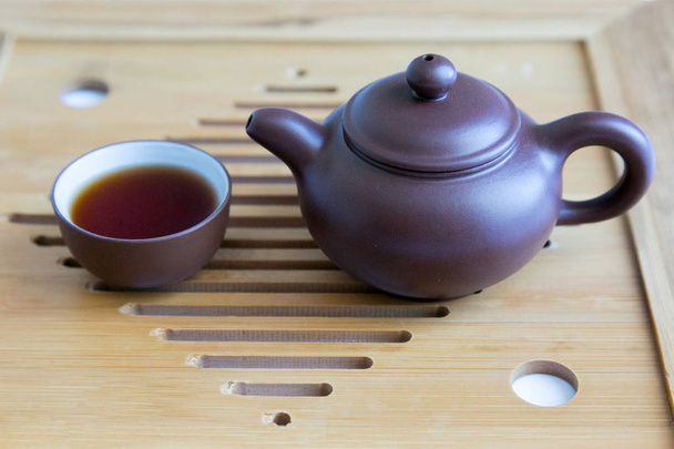 Teapot and cup made of clay on a wooden background Miniature antique tableware for tea on a wooden tray. - Fotografie, Obrázek