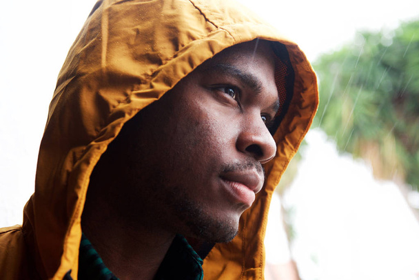 Close up portrait of young black man outdoors in the rain with raincoat  - Photo, Image