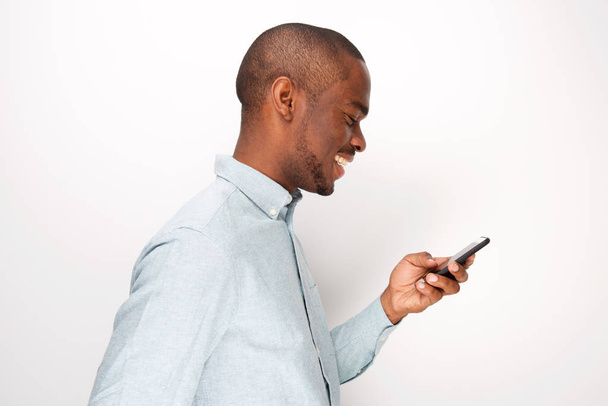 Retrato del perfil del joven negro feliz mirando el teléfono celular por el fondo blanco
 - Foto, imagen