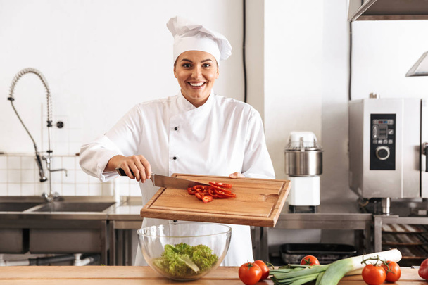 Photo of beautiful woman chef wearing white uniform making salad - Foto, imagen