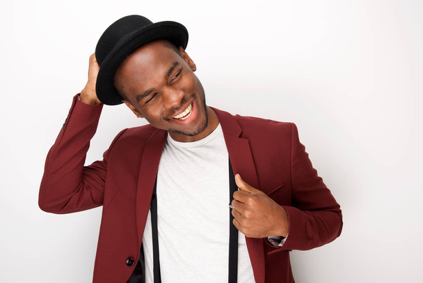 Porträt eines glücklichen afrikanisch-amerikanischen Mannes, der mit Blazer und Hut vor weißem Hintergrund posiert - Foto, Bild
