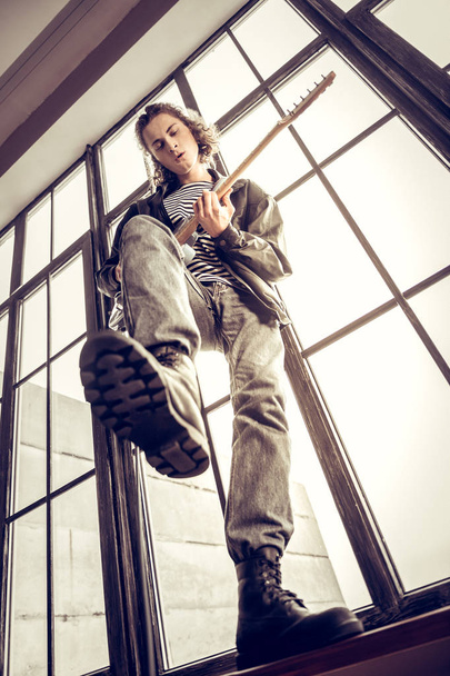 Curly rock musician raising his leg while playing hard rock music - Foto, immagini