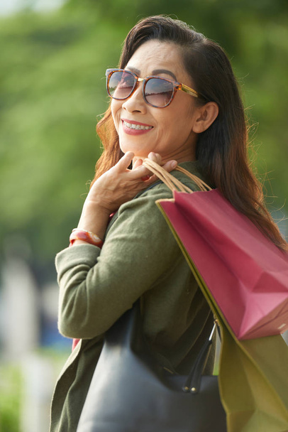 Retrato de una mujer mayor vietnamita bonita con gafas de sol sosteniendo muchas bolsas de compras
  - Foto, imagen