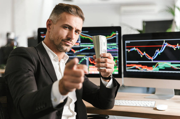 Image of adult businessman holding pack of money while working i - Foto, afbeelding