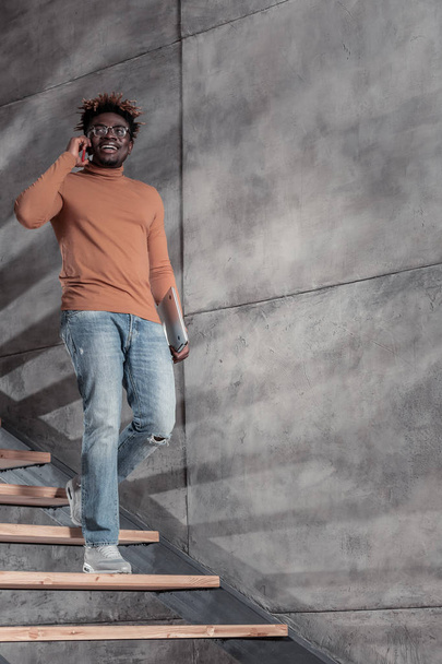 Joyful dark-skinned freelancer standing on stairs near wall - Foto, Imagen