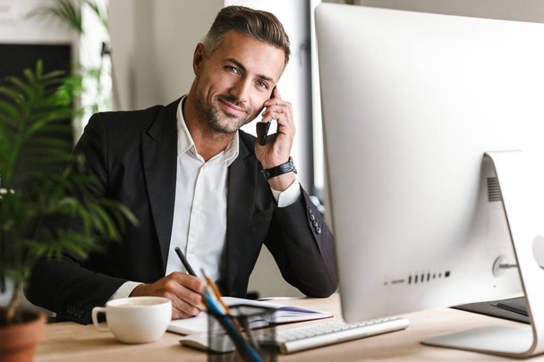 Image of happy businessman talking on cell phone while working o - Fotoğraf, Görsel
