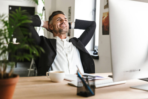 Photo of beautiful businessman smiling while sitting at desk and - Photo, image