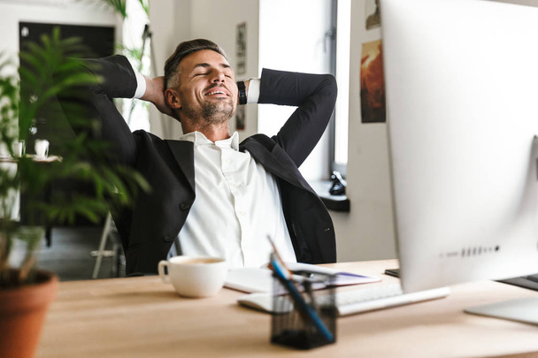 Photo of successful businessman smiling while sitting at desk an - Φωτογραφία, εικόνα