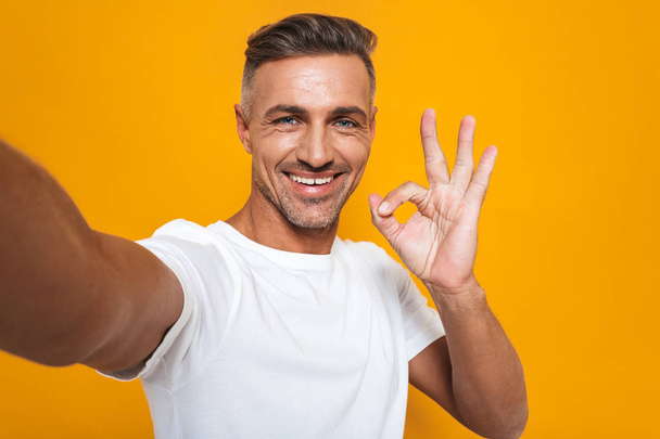 Image of brunette man 30s in white t-shirt smiling and taking se - Foto, immagini