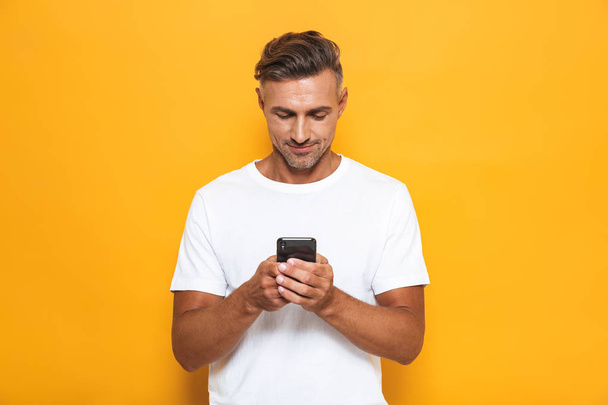 Handsome man posing isolated over yellow wall background using mobile phone. - Fotó, kép
