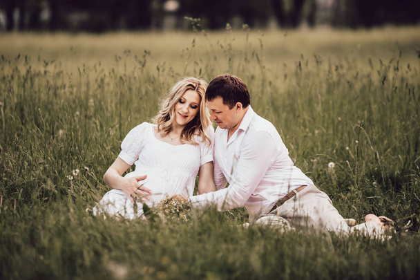 красива вагітна жінка з чоловіком сидить на газоні в літній день
. - Фото, зображення