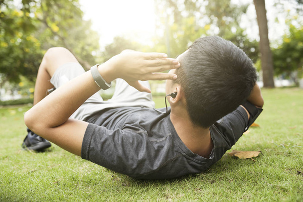 Uomo in forma attiva che indossa il fitness tracker quando fa sit-up sull'erba nel parco
  - Foto, immagini