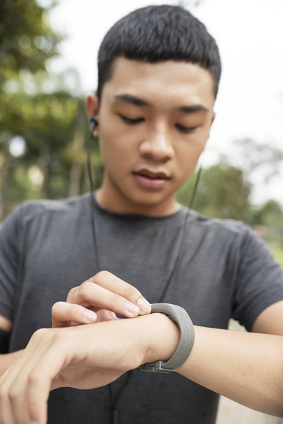 Portrait of happy young Asian man checking progress on his fitness tracker  - Foto, immagini