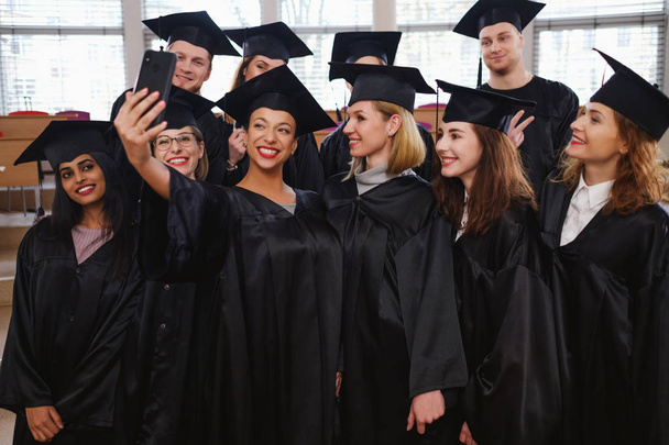 Monietninen ryhmä valmistuneiden opiskelijoiden ottaen selfie
 - Valokuva, kuva