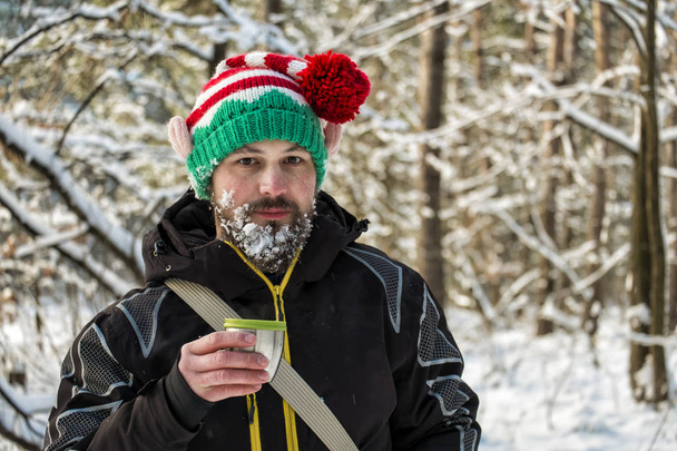 Szakállas ember egy elf kalapban az erdő gazdaság egy bögre forró tea - Fotó, kép