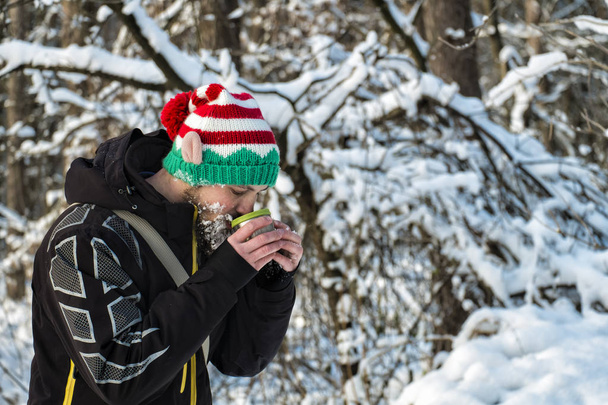 Elfo de Navidad con barba de nieve bebiendo té caliente de una taza en la helada
 - Foto, Imagen