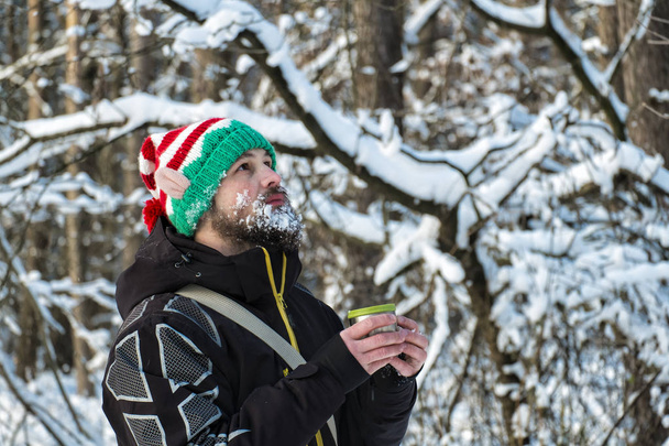 Elfo de Navidad con barba de nieve sosteniendo una taza de té caliente y mirando hacia arriba
 - Foto, Imagen