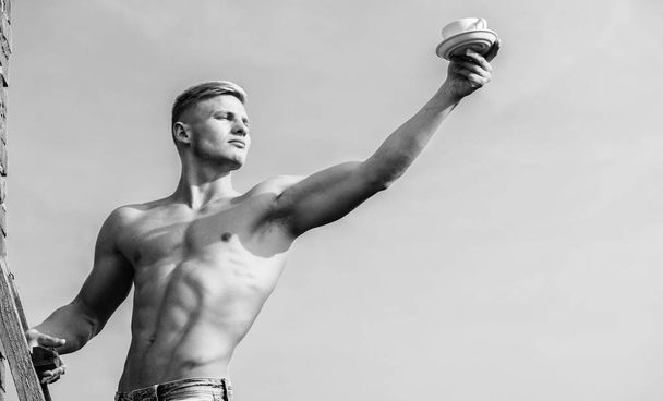Man muscular athlete bodybuilder offers you coffee. Macho muscular chest naked torso hold mug of fresh coffee blue sky background. Waiter bare chest hold coffee cup. Sexy torso attractive waiter - Foto, imagen