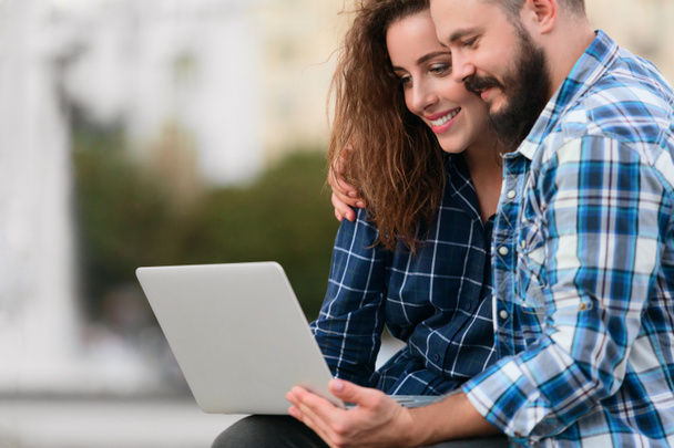 Couple heureux en utilisant un ordinateur portable assis sur le banc à l'extérieur
 - Photo, image