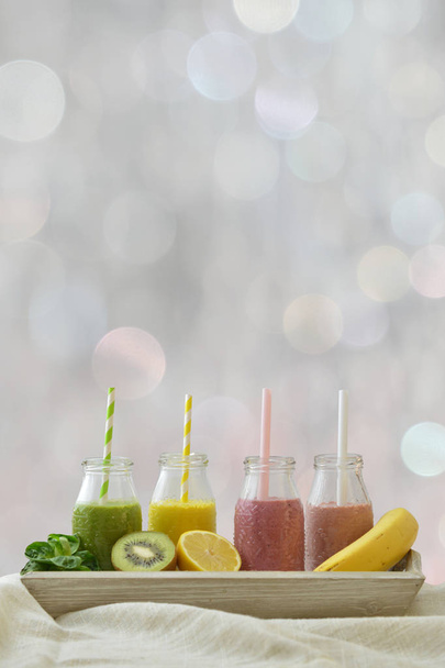 quattro frullati di frutta colorati di fila con frutta fresca di fronte a sfondo bokeh neutro con spazio copia sopra per uno stile di vita sano
 - Foto, immagini