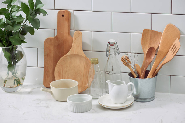 Simple rustic kitchenware against white wooden wall: rough ceramic pot with wooden cooking utensil set, stacks of ceramic bowls, jug and wooden trays. - Foto, afbeelding