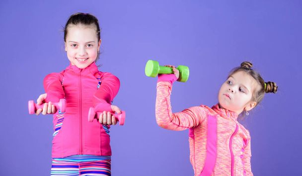 Power and energy. Little children developing physical fitness. Cute sisters doing gym fitness exercises with dumbbells. Small girls enjoy fitness training with weights. Sport and fitness for kids - Foto, Bild