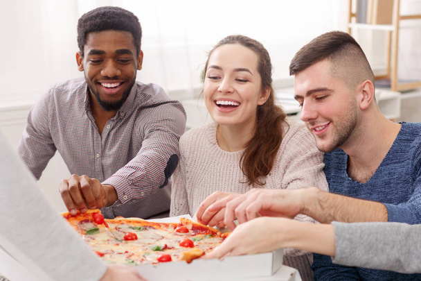Zadowoleni przyjaciele jedzą pizzę, mając stronę domową - Zdjęcie, obraz