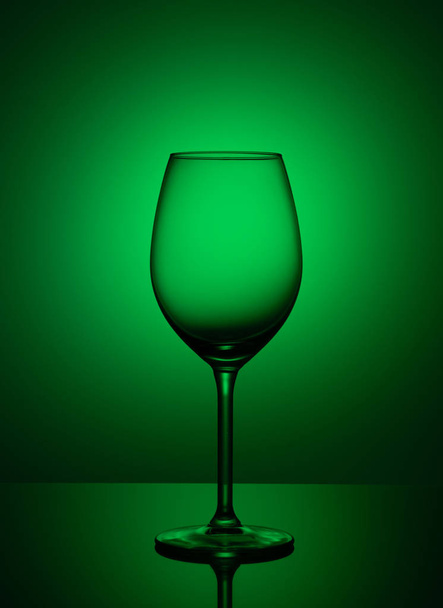 Empty wine glass stands on acrylic glass on a green background. - Фото, зображення