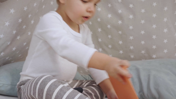 Смешной милый малыш разговаривает и играет с книгой в детском вигваме
 - Кадры, видео