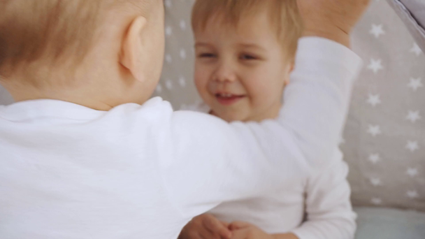 χαριτωμένο μωρό δείχνοντας με το δάχτυλο στην κάμερα και στη συνέχεια παίζοντας με μπερδεμένος αδελφός σε βρεφικό καλυβοσκηνή - Πλάνα, βίντεο